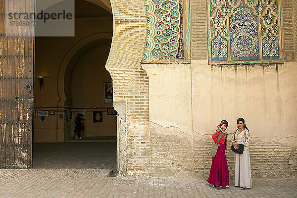 Zwei junge Frauen stehen an einer Mauer in der Nähe einer Toreinfahrt in Marokko; Meknes  Marokko