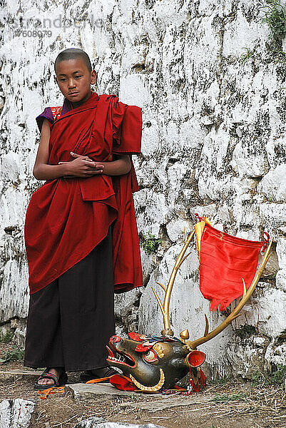 Ein junger Mönch steht neben einer Maske  die beim Paro Tshechu Festival im Paro Dzong  einem Kloster und einer Festung in Paro  Bhutan  verwendet wird; Paro  Bhutan