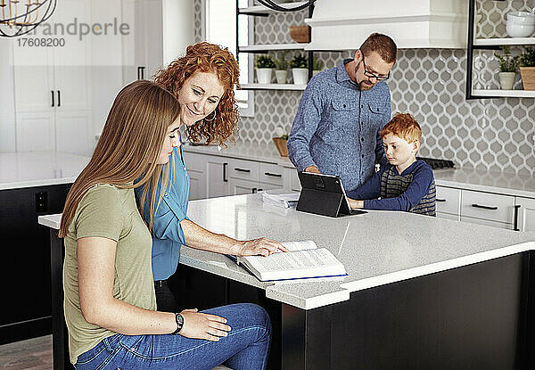Eltern helfen ihrem Sohn und ihrer Tochter im Teenageralter bei den Hausaufgaben in der heimischen Küche; Edmonton  Alberta  Kanada