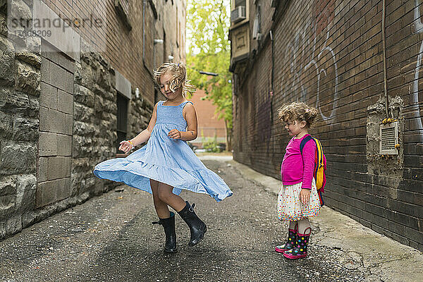 Junge Mädchen spielen zusammen in einer Gasse  das jüngste Mädchen steht da und sieht zu  wie die andere in einem Kleid herumwirbelt; Toronto  Ontario  Kanada