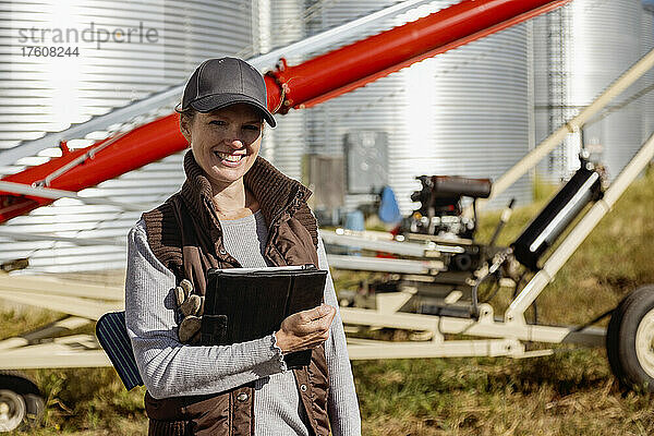 Ausschnitt aus dem Porträt einer Landwirtin  die fröhlich lächelt  während sie ein digitales Tablet in der Hand hält und auf einem modernen Bauernhof steht; Alcomdale  Alberta  Kanada