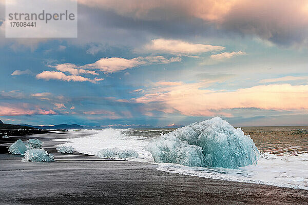 Eis aus der Gletscherlagune Jokulsarlon  das an einen schwarzen Sandstrand gespült wird  mit der sonnenbeschienenen Bergkette am Horizont; Jokulsarlon  Vatnajökull-Nationalpark  Island