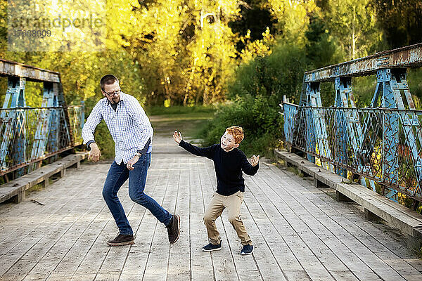 Vater und Sohn beim Tanzen auf einer Brücke in einem Park im Herbst; Edmonton  Alberta  Kanada