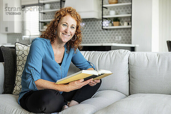 Eine mittelalte Frau sitzt zu Hause auf einer Couch  liest ein Buch und schaut in die Kamera; Edmonton  Alberta  Kanada