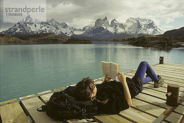 Eine Frau entspannt sich auf einem Steg und liest ein Buch; Torres del Paine National Park  Patagonien Chile.