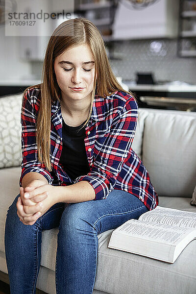 Teenager-Mädchen  das zu Hause auf einer Couch sitzt  die Bibel liest und Zeit im Gebet verbringt; Edmonton  Alberta  Kanada