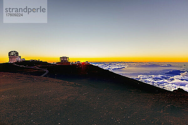 Gebäude des Haleakala-Observatoriums über den Wolken mit einem goldenen Sonnenuntergang und einem Blick auf den Ozean und die Küste darunter; Maui  Hawaii  Vereinigte Staaten von Amerika