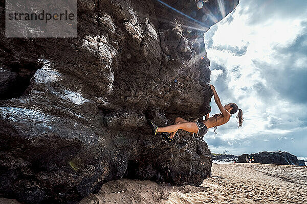 Eine Frau beim Bouldern am Strand von Hawaii.