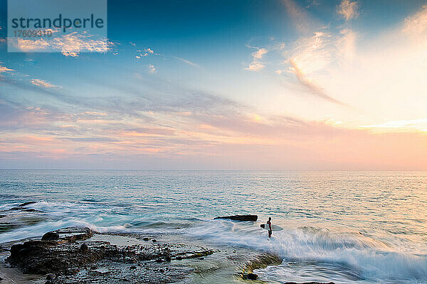 Ein Surfer  der bei Sonnenuntergang über das Riff läuft  um die Wellen zu erreichen.