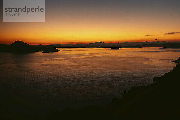 Leuchtend gelbes und orangefarbenes Glühen des Sonnenuntergangs über dem Ozean und silhouettierten Inseln im Komodo-Nationalpark im Komodo-Archipel; Ost-Nusa Tenggara  Indonesien