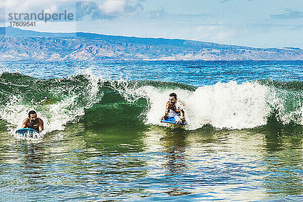 Zwei Männer fahren mit Bodyboards in den Strand am D. T. Fleming Beach mit der Insel Molokai im Hintergrund; Kapalua  Maui  Hawaii  Vereinigte Staaten von Amerika