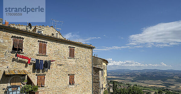 Wäsche  die zum Trocknen an der Seite eines mittelalterlichen Gebäudes in der historischen Altstadt von Volterra aufgehängt ist  mit einem Überblick über die Landschaft im Hintergrund; Volterra  Toskana  Italien