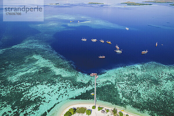 Luftaufnahme von Booten  die vor einer Insel im Komodo-Nationalpark vertäut sind  mit einem Dock  das in das umgebende türkisfarbene Wasser hineinragt; Ost-Nusa Tenggara  Kleine Sunda-Inseln  Indonesien