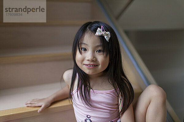 Porträt eines jungen Mädchens mit einer Haarschleife  das auf einer Treppe sitzt und in die Kamera schaut; Hongkong  China