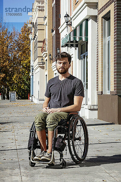 Außenporträt eines jungen querschnittsgelähmten Mannes in seinem Rollstuhl auf einem städtischen Gehweg an einem schönen Herbsttag; Edmonton  Alberta  Kanada