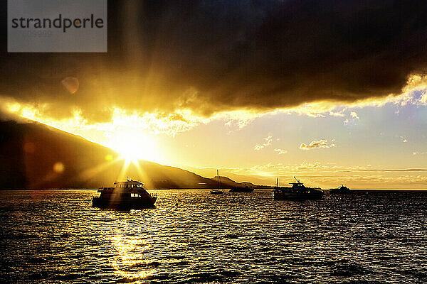 Ein goldener Sonnenuntergang hebt die Sturmwolken über den silhouettierten Yachten hervor  die im ruhigen Wasser entlang der Küste in Lahaina vertäut sind; Lahaina  Maui  Hawaii  Vereinigte Staaten von Amerika