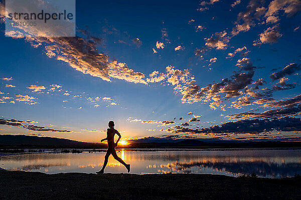 Eine Frau läuft an einem See entlang  in dem sich der Sonnenuntergang spiegelt.