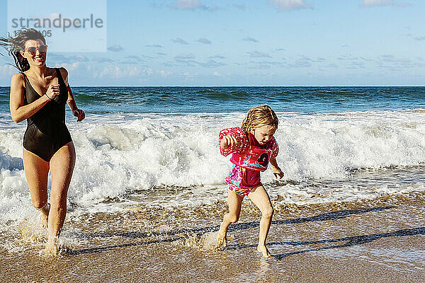 Junge Mutter spielt mit ihrer Tochter und läuft vor den Wellen am D. T. Fleming Beach weg; Kapalua  Maui  Hawaii  Vereinigte Staaten von Amerika
