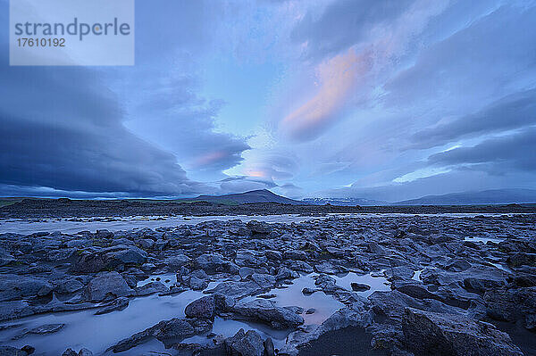 Gletscherfluss  der durch die Basaltlandschaft fließt  mit einem dramatisch bewölkten Himmel bei Sonnenuntergang im Kaldidalur-Tal; Husafell  Nordurland Vestra  Island