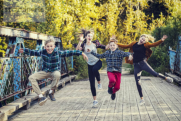 Vier Geschwister in einer Reihe springen in der Luft und machen lustige Gesten auf einer Parkbrücke; Edmonton  Alberta  Kanada