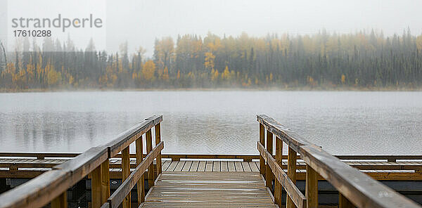 Dock am Hush Lake mit Nebel  der den herbstlich gefärbten Wald entlang des Ufers verwischt; British Columbia  Kanada