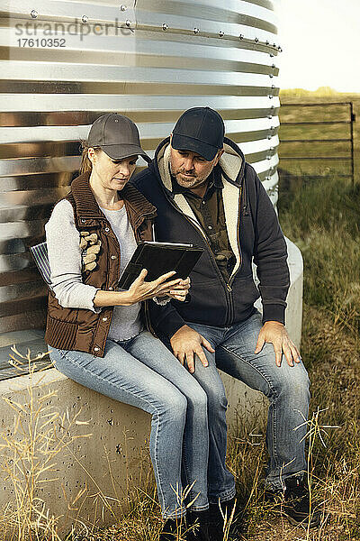 Älteres Ehepaar  das auf seinem Bauernhof arbeitet  sitzt am Rand eines Getreidespeichers und konsultiert seinen Tablet-Computer; Alcomdale  Alberta  Kanada