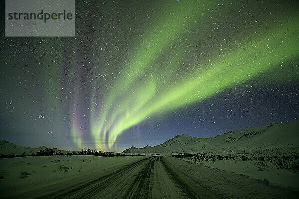 Aurora borealis (oder Nordlicht) am Sternenhimmel über dem Dempster Highway und den schneebedeckten Bergen im Winter; Yukon  Kanada