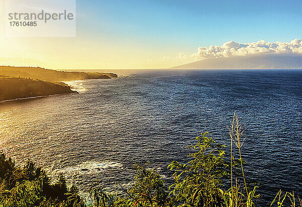 Die zerklüftete Küstenlinie von Nord-Maui  bedeckt mit üppigem  grünem Laub und der untergehenden Sonne über dem Meer mit der Insel Molokai am Horizont; Maui  Hawaii  Vereinigte Staaten von Amerika