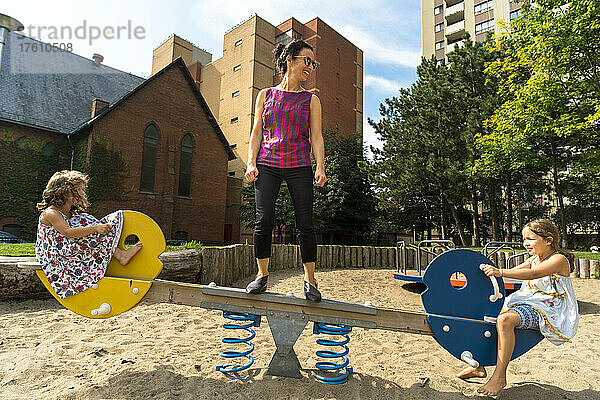 Junge Schwestern mit ihrer Mutter spielen zusammen auf einer Wippe auf einem Spielplatz; Toronto  Ontario  Kanada