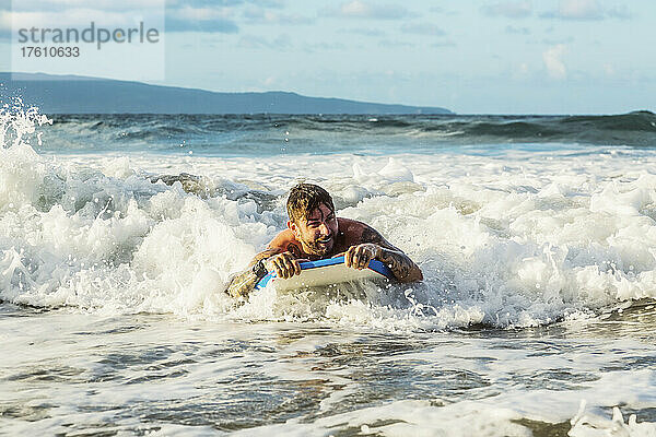 Nahaufnahme eines Mannes  der auf einem Bodyboard eine Welle in den Strand von D. T. Fleming Beach reitet  mit der Insel Molokai im Hintergrund; Kapalua  Maui  Hawaii  Vereinigte Staaten von Amerika