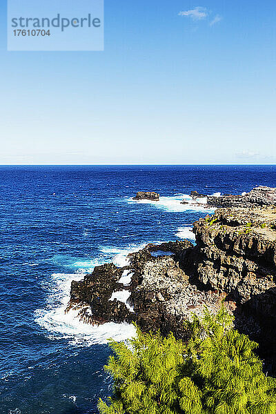 Blick auf den Ozean und den Horizont am Nakalele Point vor einem blauen Himmel mit der zerklüfteten  felsigen Küste und tropischen Blättern im Vordergrund; Maui  Hawaii  Vereinigte Staaten von Amerika