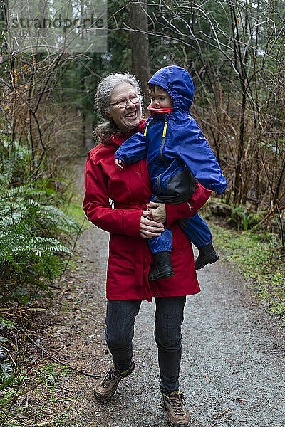 Großmutter hält ihre Enkelin im Vorschulalter im Arm  während sie einen Waldweg entlanglaufen; North Vancouver  British Columbia  Kanada