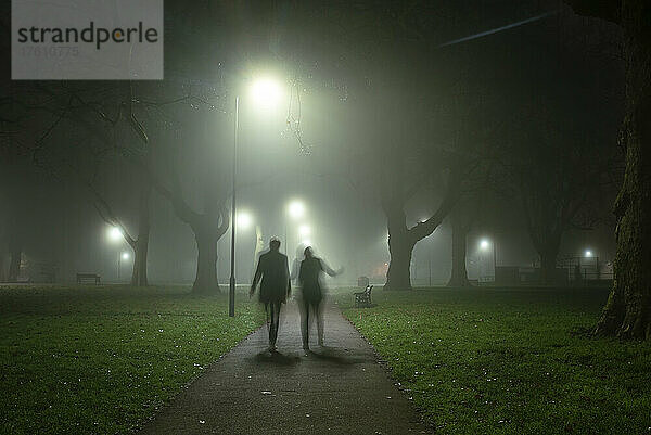 Bewegungsunschärfe und Silhouette von zwei Personen  die an einem nebligen Morgen in London Fields  Shoreditch  London  UK  spazieren gehen; London  England