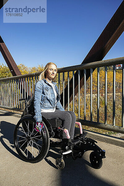 Junge querschnittsgelähmte Frau  die an einem schönen Herbsttag in ihrem Rollstuhl über eine Brücke fährt; Edmonton  Alberta  Kanada