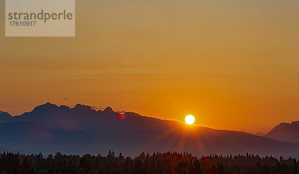 Goldener Sonnenuntergang hinter den Bergen mit Sonnenstrahlen  die über einen Wald fluten; Surrey  British Columbia  Kanada
