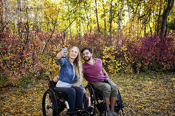 Ein junger querschnittsgelähmter Mann und eine Frau in ihren Rollstühlen machen ein Selbstporträt mit einem Smartphone in einem Park an einem schönen Herbsttag; Edmonton  Alberta  Kanada