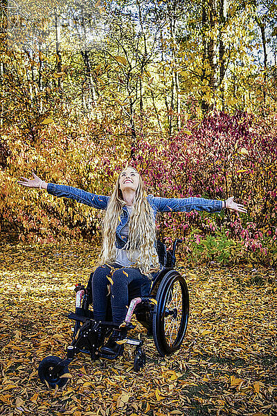 Eine junge querschnittsgelähmte Frau in ihrem Rollstuhl in einem Park an einem schönen Herbsttag  die Arme ausgestreckt und die freie Natur genießend; Edmonton  Alberta  Kanada
