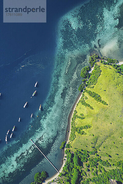 Blick von oben auf Boote  die vor einer Insel im Komodo-Nationalpark vertäut sind  mit einem Steg  der in das türkisfarbene Wasser hineinragt; Ost-Nusa Tenggara  Kleine Sunda-Inseln  Indonesien