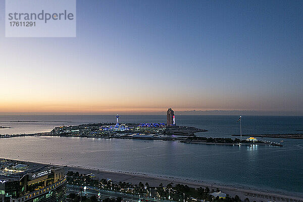 Die Sonne geht hinter Marina Island am Persischen Golf in Abu Dhabi  Vereinigte Arabische Emirate  unter. Ein Vergnügungspark erstrahlt in der Abenddämmerung  während das noch nicht eröffnete Atlantis-Hotel schlummert; Abu Dhabi  Vereinigte Arabische Emirate