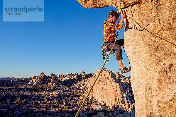 Ein Kletterer nimmt bei Sonnenuntergang einen Überhang über dem Hidden Valley im Joshua Tree National Park in Angriff.