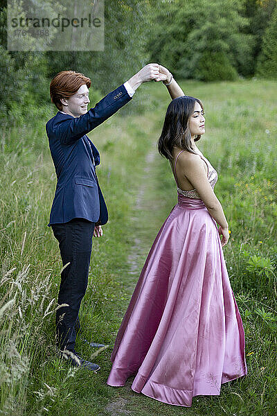 Junges Paar tanzt in formeller Kleidung auf einem abgenutzten Weg in einem Park  Abschlussfoto-Shooting in Green Timbers Urban Forest; Surrey  British Columbia  Kanada