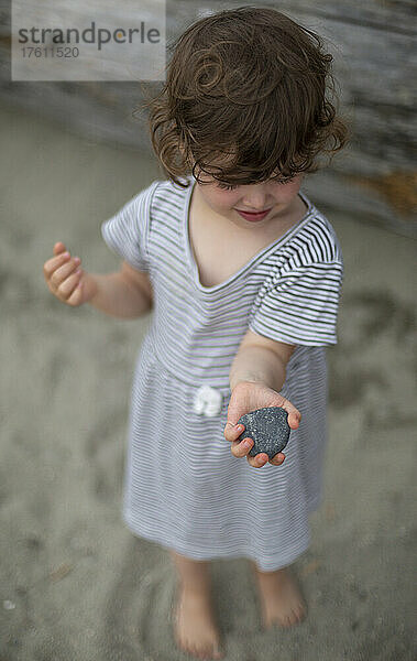 Mädchen im Vorschulalter steht auf dem Sand eines Strandes und hält einen Stein  Ambleside Beach in West Vancouver  BC  Kanada; West Vancouver  British Columbia  Kanada