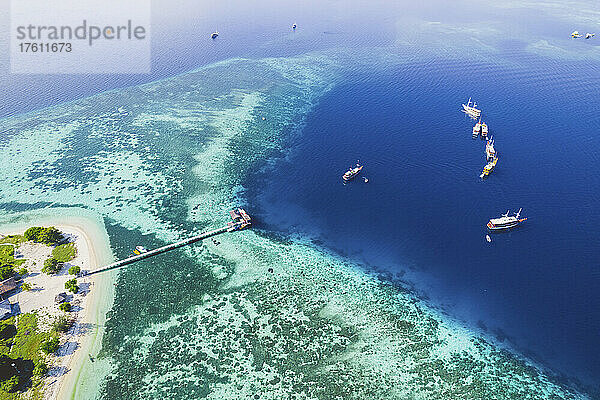 Luftaufnahme von Booten  die vor einer Insel im Komodo-Nationalpark vertäut sind  mit einem Dock  das in das umgebende türkisfarbene Wasser hineinragt; Ost-Nusa Tenggara  Kleine Sunda-Inseln  Indonesien