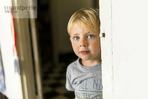 Junge mit blauen Augen  der hinter einer Mauer in die Kamera schaut; Vientiane  Präfektur Vientiane  Laos