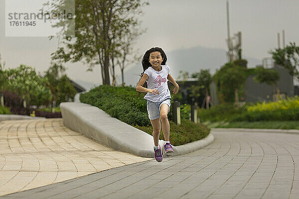 Junges Mädchen mit langen Haaren  das einen Parkweg entlangläuft und in die Kamera schaut; Hongkong  China
