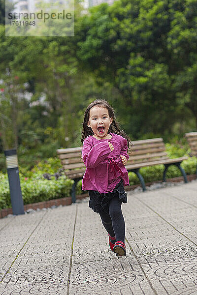 Junges Mädchen läuft im Freien in einem Stadtpark auf die Kamera zu; Hongkong  China