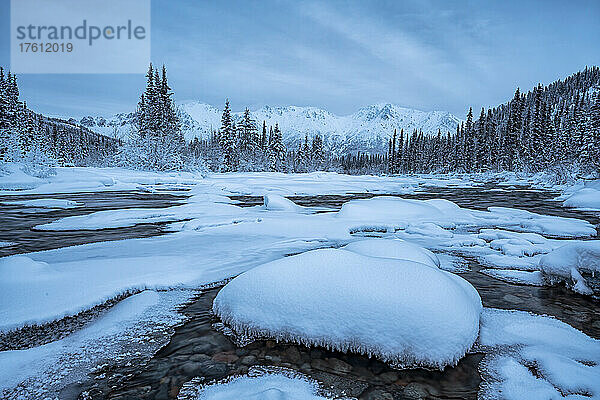 Schneebedeckte  von Eis umrandete Felsen am Wheaton River bei Sonnenaufgang mit den Bergen in der Ferne; Whitehorse  Yukon  Kanada