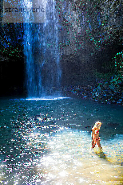 Eine junge Frau in einem natürlichen Becken am Fuße eines Wasserfalls.