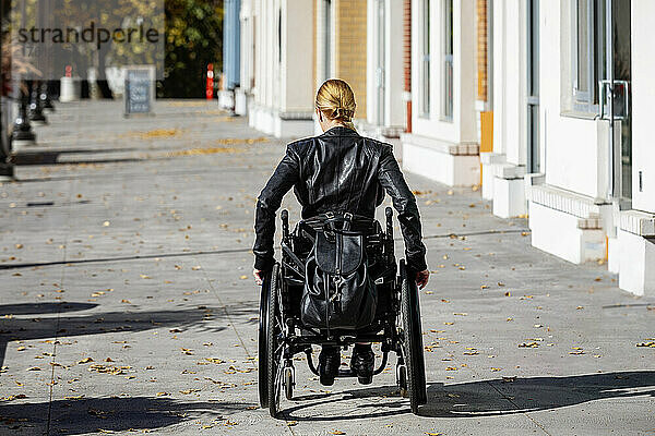 Junge querschnittsgelähmte Frau in ihrem Rollstuhl  die an einem schönen Herbsttag einen städtischen Gehweg hinunterfährt; Edmonton  Alberta  Kanada