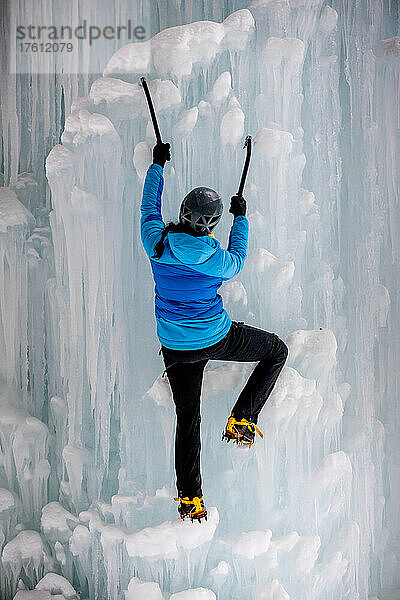 Eine Frau klettert mit Eispickel und Steigeisen durch eine Eiswand.